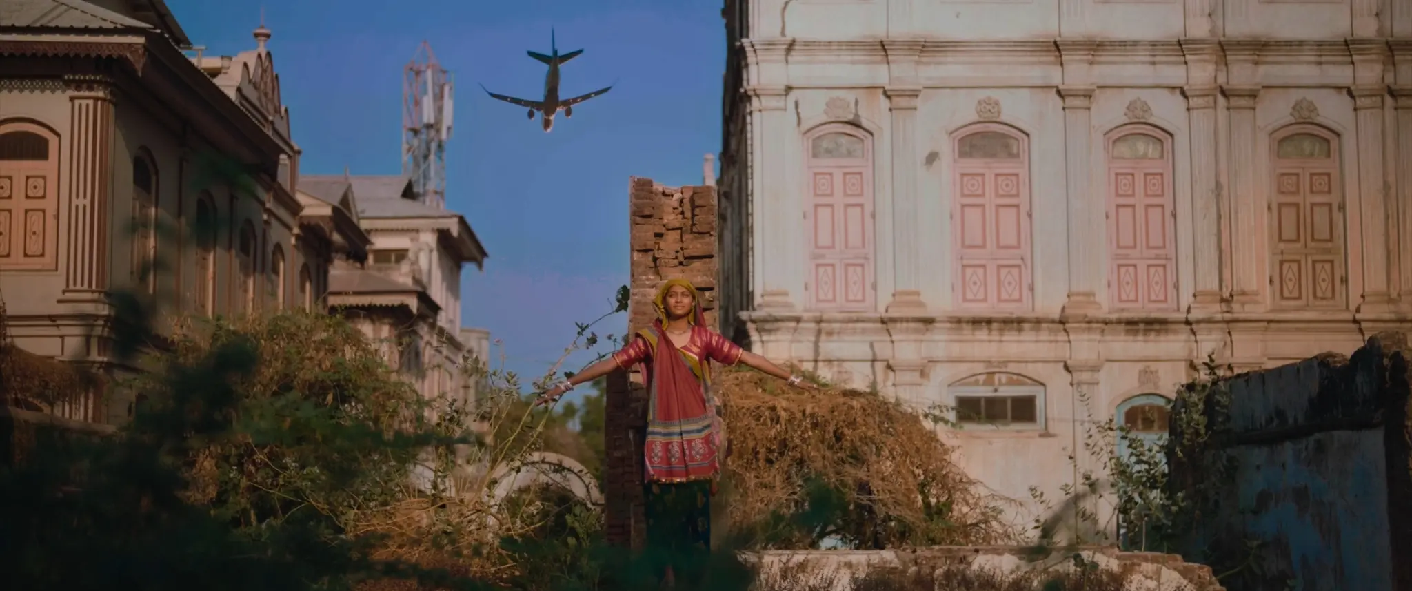 A woman standing between historic buildings as an aircraft passes overhead